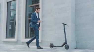 Takım Elbiseli İşadamı akıllı telefonuyla elektrikli scooter 'ı çalıştırıyor. QR kodunu tarıyor. Modern Girişimci Ofis Toplantısına Çağdaş Ekolojik Taşımacılık Kullanıyor.