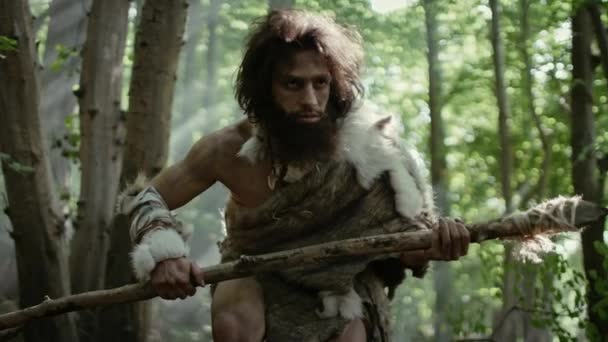 Porträt eines Höhlenmenschen mit Tierhaut und Pelz auf der Jagd mit einem steinernen Speer im Urwald. Urzeitlicher Neandertaler-Jäger bereit, Speer in den Dschungel zu werfen