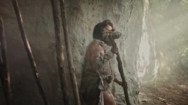 Hayvan Derisi Giyen Primeval Caveman Taş Uçlu Çekiç Tutar Mağara dan çıkar ve Prehistorik Orman Etrafında Bakar, Hayvan Prey Hunt hazır. Neandertal Ormana Avlanmaya Gidiyor. Yay Atış