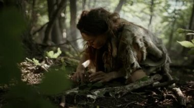 Tarih öncesi mağara kadını avcı-toplayıcı ormanda fındık ve dut arıyor. İlkel Neandertal Kadın Güneşli Ormanda Yiyecek Buluyor