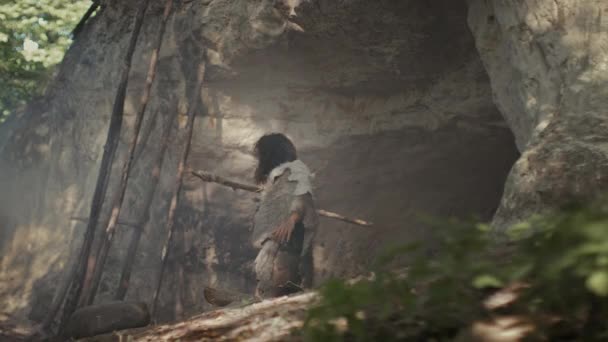 動物の皮と毛皮を身に着けている原始的な洞窟人は、石の先端の槍を持っています彼の洞窟から先史時代の森狩りの準備ができて出てきます。ネアンデルタール人がジャングルに狩りに行く — ストック動画