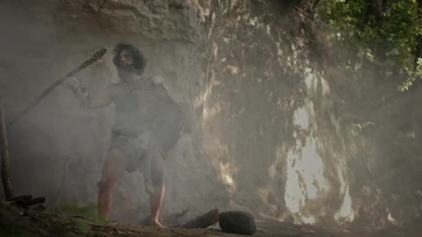 Ur-Höhlenmensch mit Tierhaut und Pelz hält steingekippten Speer in der Hand und kommt aus seiner Höhle in den Urwald. Neandertaler auf Jagd in den Dschungel — Stockvideo