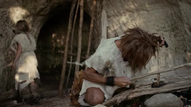 Urzeit-Höhlenmensch mit Tierfell versucht mit Bogenbohrmethode ein Feuer zu machen. Neandertaler entzünden das erste menschengemachte Feuer in der Geschichte der menschlichen Zivilisation. Feuer machen zum Kochen. Zoom in Schuss