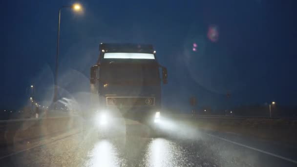 Blue Long Haul Semi-Truck with Cargo Trailer Full of Goods Travels At Night on the Freeway Road, Driving Across Continent Through Rain, Fog, Snow. Промисловий район. Передня частина після пострілу — стокове відео