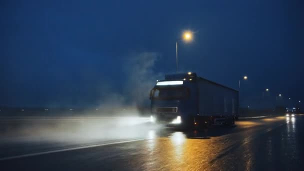 貨物トレーラー付きブルーロングホールセミトラック貨物の完全な雨、霧、雪を介して大陸を横断運転、高速道路の夜に旅行します。工業用倉庫エリア。ショット後のフロント — ストック動画