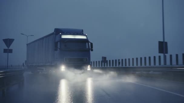 Semi-camion long-courrier avec remorque pleine de marchandises voyage sur la route de la route. Conduire tôt le matin à travers le continent à travers la pluie, le brouillard. Zone des entrepôts industriels. Front suivant tir au ralenti — Video