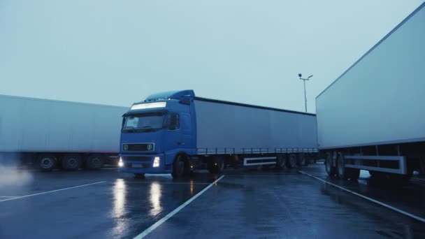 Blue Semi-Truck teherautóval behajt a parkolóba, ahol más teherautók állnak. Ipari logisztikai terület. Berakodási vagy kirakodási hely a távolsági teherautók számára. Oldalnézet Arc lövés