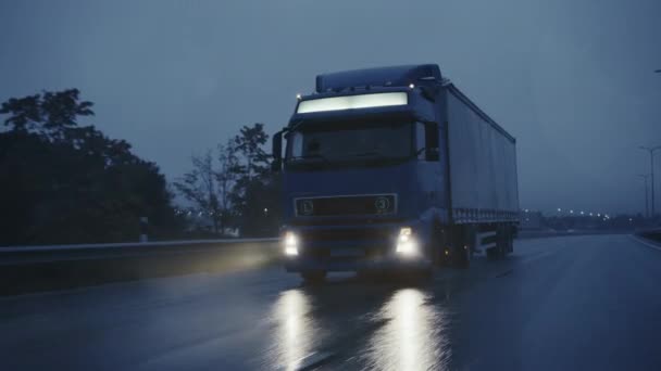 Длинный полугрузовик с грузовым прицепом, полным гудков, на шоссе. Ехать ранним утром по всему континенту сквозь дождь, туман. Промышленные склады. Передняя камера обгона — стоковое видео