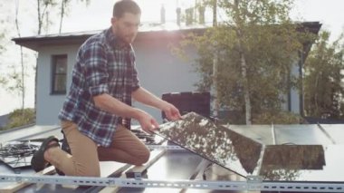 Checkered Shirt 'teki beyaz adam Metal Basis' in üzerine siyah yansıtıcı güneş panelleri kuruyor. Güneşli bir günde, bir çatı katında çalışıyor. Ekolojik Yenilenebilir Enerji Konsepti.