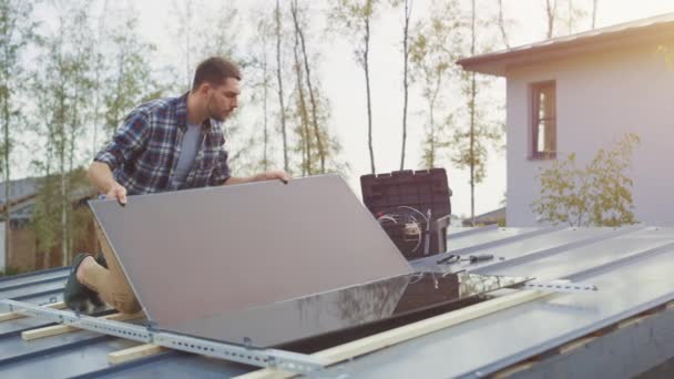 L'homme caucasien en chemise à carreaux installe des panneaux solaires réfléchissants noirs sur une base métallique. Il travaille sur un toit de maison par une journée ensoleillée. Concept d'énergie renouvelable écologique à la maison. — Video