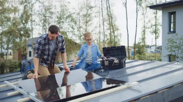 Ojciec i Syn Instalują panele słoneczne na metalowej podstawie z wiertłem. Pracują na dachu domu w słoneczny dzień i przybij piątkę. Koncepcja ekologicznej energii odnawialnej w domu i jakości czasu rodzinnego. — Wideo stockowe
