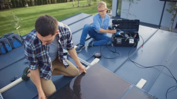 Vader en Zoon installeren zonnepanelen op een metalen basis. Ze werken met Bedrading op een dak op een zonnige dag. Begrip ecologisch hernieuwbare energie thuis en in het gezin van hoge kwaliteit. — Stockvideo