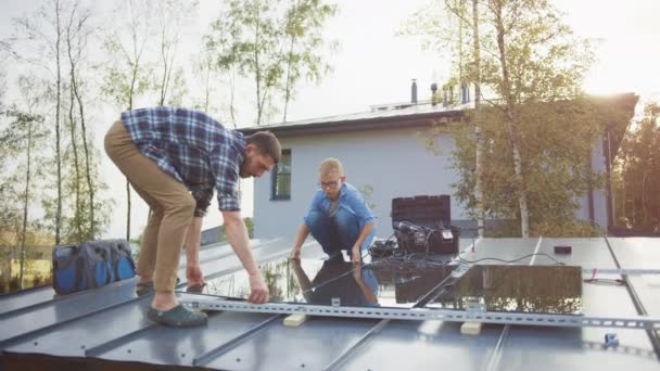 Padre e hijo instalando paneles solares en una base metálica con un taladro. Trabajan en un tejado de la casa en un día soleado y High Five. Concepto de Energía Renovable Ecológica en el Hogar y Tiempo Familiar de Calidad. — Vídeo de stock