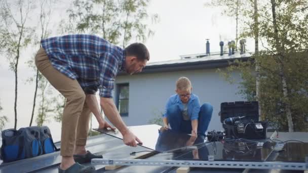 Padre e Hijo Instalando Paneles Solares a una Base Metal. Están sosteniendo los paneles en un tejado de la casa en un día soleado. Concepto de Energía Renovable Ecológica en el Hogar y Tiempo Familiar de Calidad. — Vídeos de Stock