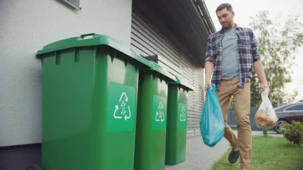 Caucasian Man is Walking Outside His House in Order to Take Out Two Plastic Bags of Trash. One Garbage Bag is Sorted into Biological Food Waste, Other is Thrown into Recyclable Bottles Garbage Bin. — ストック動画