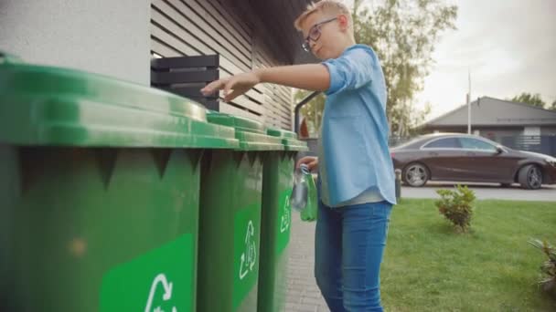 Мальчик выходит из своего дома, чтобы выбросить две пустые пластиковые бутылки в мусорный бак. Он использует правильный мусорный бак, потому что эта семья сортирует отходы и помогает окружающей среде. — стоковое видео