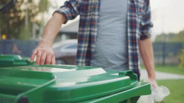 Close Up Shot of a Caucasian Male in Checkered Shirt Throwing Away Biological Food Waste into a Green Trash Bin. He Uses Correct Garbage Bin Because He is Sorting Waste and Helping the Environment.