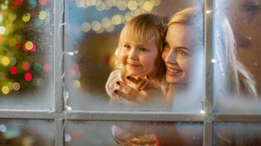 Noel arifesinde anne ve kızı pencereden bakıyor. Pencerede Çiçek Parlıyor.