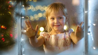 Noel arifesinde sevimli küçük kız pencere ve gülümsüyor arar.