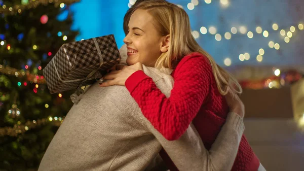 Mulher bonita feliz abraça seu homem bonito depois de receber um presente. Árvore de Natal e Confetti voador no fundo . — Fotografia de Stock