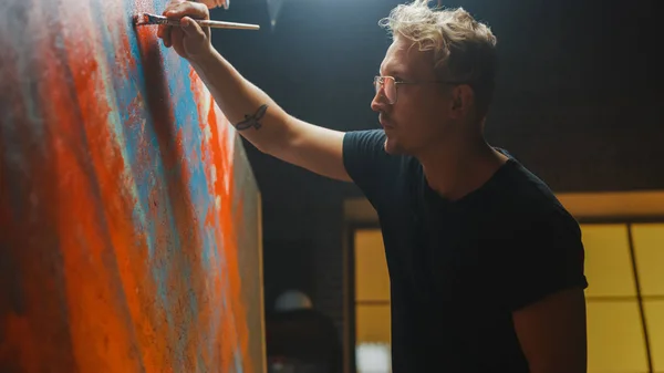 Artista talentoso que trabaja en la pintura abstracta, se sumerge en la pintura y comienza a dibujar arte moderno audazmente emocional. Estudio creativo oscuro grandes soportes de lona en caballete iluminado — Foto de Stock