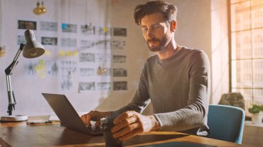 İçişleri Bakanlığı Stüdyosunda Masasında Oturan Profesyonel Yaratıcı Bir Dizüstü bilgisayar üzerinde çalışıyor, Çay ya da Kahve ile Kupa Tutuyor.