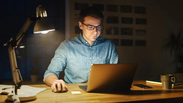 Ein professioneller Mann sitzt abends an seinem Schreibtisch im Bürostudio und arbeitet an einem Laptop. Mann analysiert Statistik. — Stockfoto