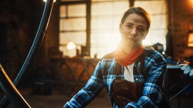 Kulak delen Genç Güzel Kadın kameraya nazikçe gülümsüyor. Metal atölyesinde İş Giysileri Giyen Otantik Fabrikatör.