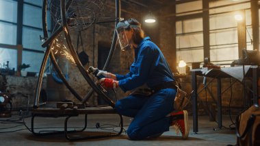 Mavi Tulumlu Genç Çağdaş Kadın Sanatçı, Stüdyo atölyesinde Bir Angle Grinder ile Metal Metro Heykeli Öğütüyor. Güçlendirici Kadın Metalden Modern Vahşi Sanatsal Çalışmalar Yapıyor.