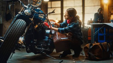 Young Beautiful Female Mechanic is Working on a Custom Bobber Motorcycle. Talented Girl Wearing a Checkered Shirt and an Apron. She Uses a Spanner to Tighten Nut Bolts. Authentic Workshop Garage. clipart