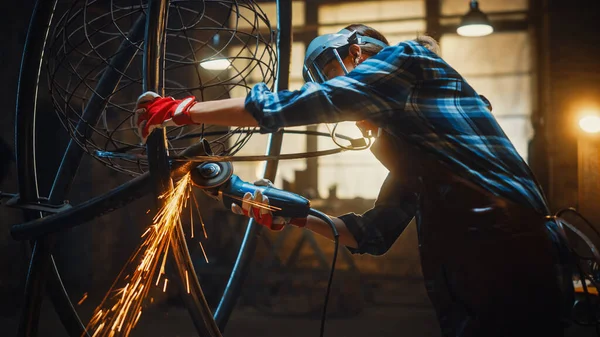 Schöne Künstlerin benutzt einen Winkelschleifer, um brutale Metallskulpturen im Atelier zu machen. Tomboy Girl poliert Metallrohr mit Funken, die abfliegen. Zeitgenössischer Fabrikator schafft abstrakte Stahlkunst. — Stockfoto