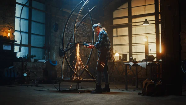 Talent Innovative Female Artist cammina verso una scultura in tubo metallico, accende e utilizza un smerigliatrice angolare in un laboratorio. Produttore contemporaneo Creazione di arte moderna in acciaio . — Foto Stock