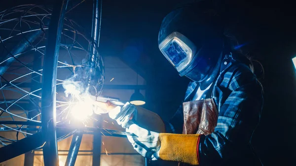 Talangfull innovativ Tomboy kvinnlig konstnär i en rutig skjorta svetsar en abstrakt, brutal och uttrycksfull metallskulptur i en verkstad. Samtida Fabricator Skapa modern stålkonst. — Stockfoto