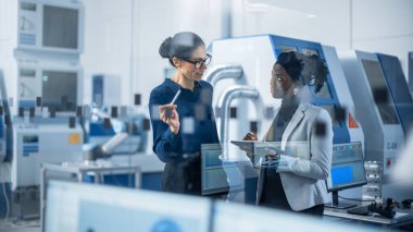 Endüstriyel Mühendis Proje Yöneticisi ile konuşuyor, Dijital Tablet Bilgisayar kullanıyorlar ve Modern Fabrika Planlama 'yı tartışıyorlar. CNC Makineleri ve Robot Silahlanma Hattı ile Üretim Tesisi