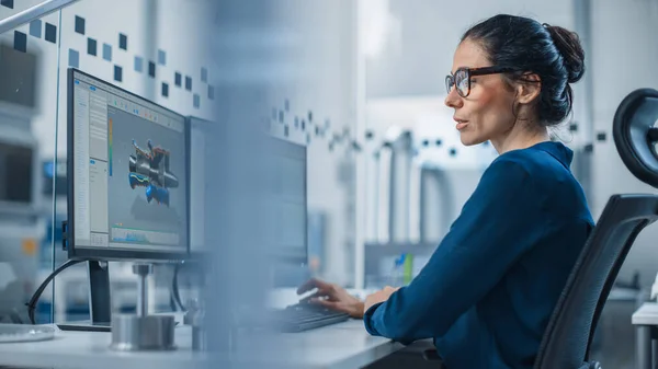 Ingegnere donna industriale Lavorando su un personal computer, due schermi monitor mostrano software CAD con prototipo 3D di nuovo motore ibrido a idrogeno e grafici. Fabbrica moderna con macchinari ad alta tecnologia — Foto Stock