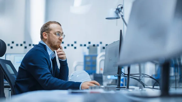 Shot of Male Industrial Engineer Løsning Problemer, Arbejder på en personlig computer, Han arbejder i Office i moderne fabrik med High-Tech Maskiner. - Stock-foto