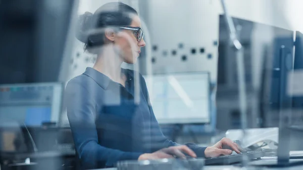 Skjuten genom glas. Kvinnlig ingenjör som arbetar med persondator. Hon arbetar på kontoret i Modern Factory med högteknologiska maskiner. — Stockfoto