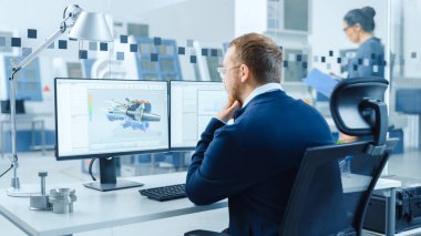 Bir Kişisel Bilgisayar üzerinde çalışan Endüstriyel Mühendis, İki Monitör, Melez Elektrik Motoru ve Haritaları 'nın 3 boyutlu prototipiyle CAD yazılımını gösteriyor. Çalışan Modern Fabrika.
