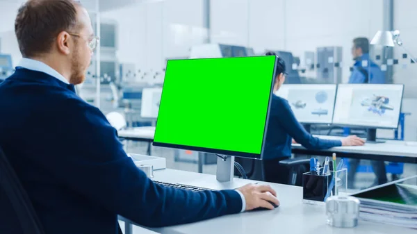 Über die Schulter: Schwerindustrie-Ingenieur, der am Personal Computer arbeitet, Display ist ein grüner Mock-up-Bildschirm oder Chroma Key. Industrielle Fabrik mit High-Tech CNC-Maschinen — Stockfoto