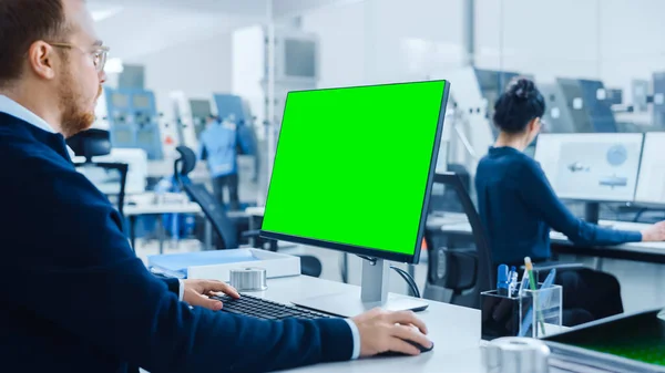 Sobre el hombro: Ingeniero de la industria pesada Trabajando en el ordenador personal, la pantalla es Verde Mock-up Screen o Chroma Key. Fábrica industrial con maquinaria CNC de alta tecnología, profesionales trabajando —  Fotos de Stock