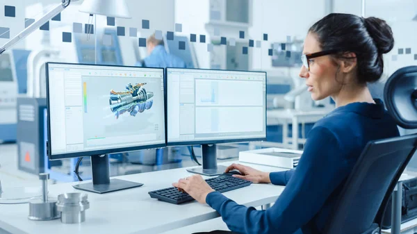 Industrial Female Engineer Werken op een personal computer, twee monitor schermen tonen CAD-software met 3D Prototype van de motor en grafieken. Moderne fabriek met high-tech machines — Stockfoto