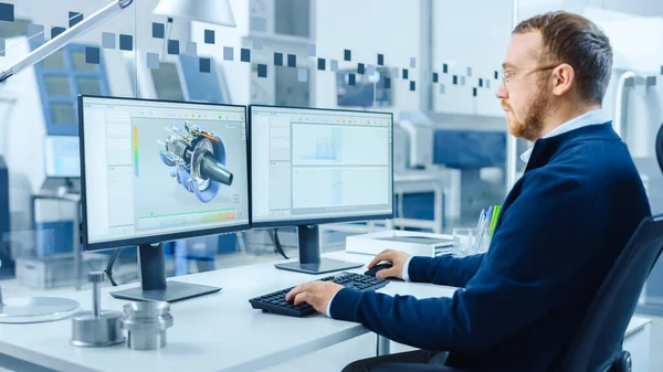 Ingeniero industrial Trabajando en una computadora personal, dos pantallas de monitor muestran software CAD con prototipo 3D de motor eléctrico híbrido y gráficos. Fábrica moderna con maquinaria de alta tecnología — Foto de Stock