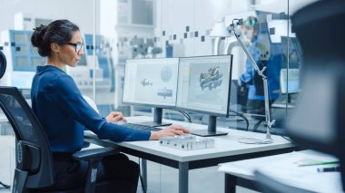 Kadın Endüstriyel Mühendislik Çözme Sorunları, Kişisel Bilgisayarda Çalışan, İki Monitör CAD Yazılımını 3 Boyutlu Test Edilen Motor Prototipi ile gösteriyor. Çalışan Modern Fabrika
