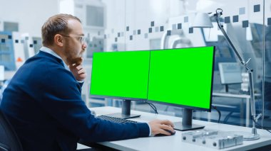 Endüstriyel Mühendis Kişisel Bilgisayar, İki Monitör Model, Yeşil Ekran, Krom Anahtar Ekranları üzerinde çalışıyor. Yüksek Teknoloji Makineli Modern Fabrika