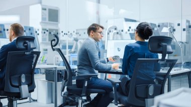 Modern Fabrika: Kadın Proje Yöneticisi Bilgisayar 'da çalışan bir erkek endüstriyel mühendis ile konuşuyor. Tasarım ve Geliştirme için CAD Yazılım kullanıyorlar. Arka planda Yüksek Teknoloji Endüstriyel Malzemeler