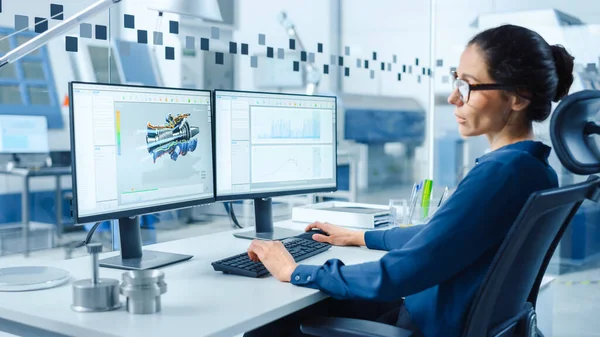 Ingeniera industrial femenina resolviendo problemas, trabajando en un ordenador personal, dos pantallas de monitor muestran software CAD con prototipo 3D de motor de cero emisiones que se está probando. Fábrica moderna de trabajo —  Fotos de Stock