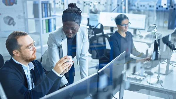 Modern Factory: La supervisora del proyecto habla con un ingeniero industrial masculino que trabaja en la computadora. Inspeccionan el mecanismo de maquinaria y diseñan la versión mejorada. Instalación industrial de alta tecnología de trabajo — Foto de Stock