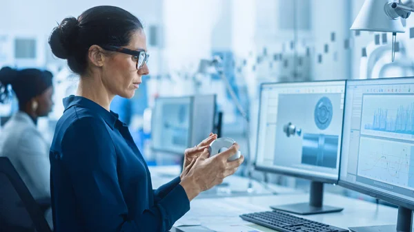 Engenheira Feminina Trabalhando em Computador Pessoal, Inspecionando Modelo de Mecanismo de Máquinas Industriais. Ela trabalha com a equipe de profissionais industriais em escritório que está localizado na fábrica moderna de trabalho — Fotografia de Stock