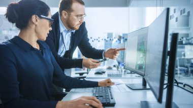 Modern Elektronik Fabrikası: CAD Yazılım ile Bilgisayar üzerine çalışan Kadın Elektrik Mühendisi ile Erkek Denetçi Konuşuyor. PCB, Mikroçipler, Yarı iletkenler ve Telekomünikasyon Ekipmanları Geliştiriliyor