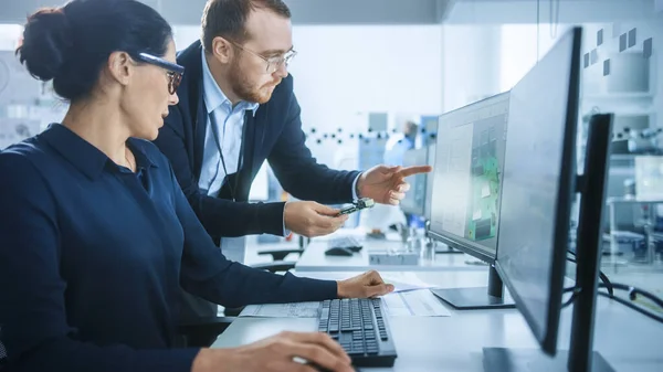 Modern Electronics Factory: Supervisor Masculino Fala com uma Engenheira Elétrica Feminina que Trabalha em Computador com Software CAD. Desenvolvimento de PCB, Microchips, Semicondutores e Equipamentos de Telecomunicações — Fotografia de Stock